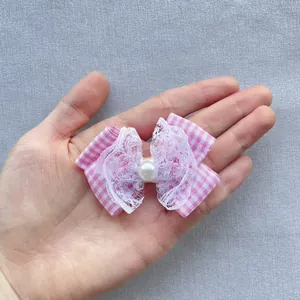 Detailed close-up of handmade pink plaid bow with white lace and pearl on palm