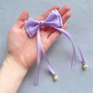 Detail van paarse satijnen strik haaraccessoire met hangende linten en parelhanger