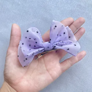 Detail of purple mesh bow hair clip with black polka dots held in hand for size reference