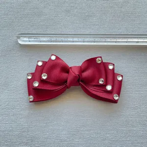 Detail of burgundy grosgrain ribbon bow with rhinestones next to a measuring ruler