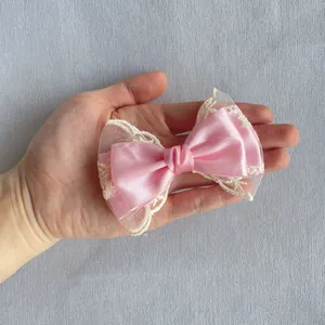Nœud en satin rose avec bordure en dentelle blanche présenté en main pour l'échelle