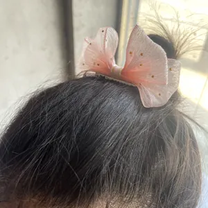 Detailed view of a pink tulle bow hair clip with gold dots worn on a child's dark hair