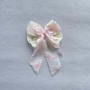 Détail d'un nœud en dentelle florale avec rubans rose pastel et perle centrale nacrée