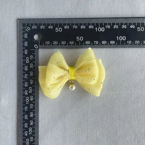Macro view of a yellow gauze bow hair accessory with pearl charm and rhinestones