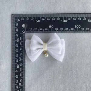 Detail of white glitter fabric bow with pearl pendant and yellow ribbon center