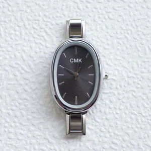 Macro shot of a minimalist oval dark grey dial with silver steel link strap and CMK logo