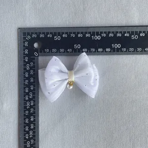Close-up of white organza bow with rhinestones and pearl detail next to a ruler