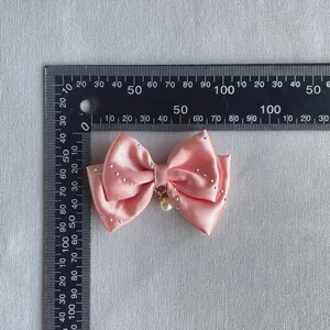 Detail of pink satin ribbon bow with rhinestones and white pearl pendant for DIY hair crafts
