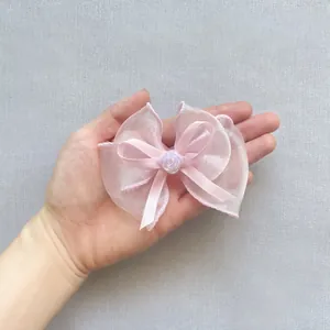 Makroaufnahme einer rosa Organzaschleife mit Perlenrose in der Hand gehalten