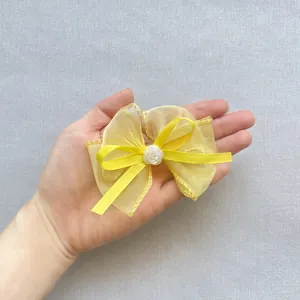 Gelbe Organzaschleife mit Goldnähten und Blumen-Detail auf der Hand präsentiert