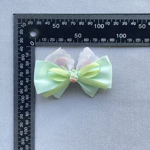Detailed view of floral bow hair accessory with strawberry charm on a measurement grid