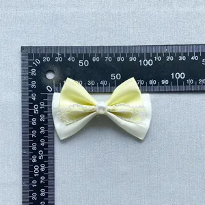 Handmade yellow and white crystal bow accessory with pearl center on gray textured fabric