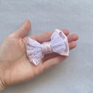Dettaglio di un fiocco per capelli in tessuto glitter rosa e pizzo bianco nella mano