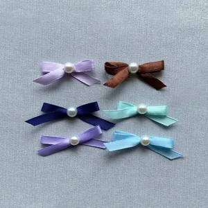 Close-up of handmade satin bow cake toppers with pearls in six assorted pastel colors