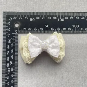 Detail view of beige fabric bow with lace trim and small white rose on a measuring scale