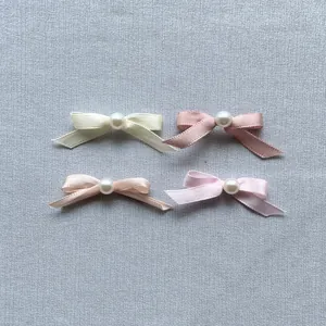 Detailed view of four satin bow cake toppers with pearls in assorted pastel colors