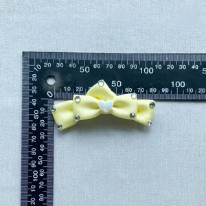 Pale yellow satin bow accessory with rhinestones and heart detail on blue background