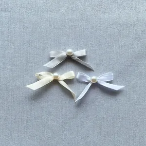 Detailed view of three satin ribbon bows with pearl centers in grey, beige, and white colors