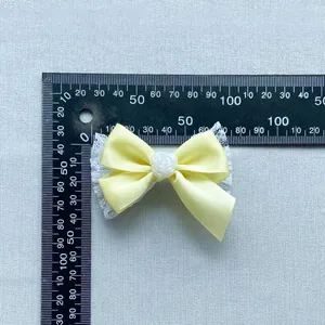 Detail of yellow silk ribbon bow with white lace base and resin rose for DIY crafts