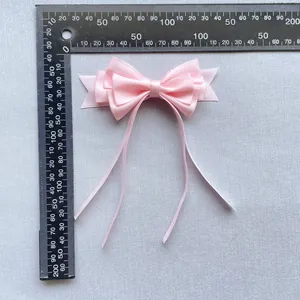 Nœud en satin rose avec rubans et règle mesurant les dimensions de 85mm sur 140mm