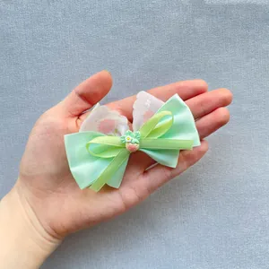 Close-up of floral bow hair accessory with strawberry detail held in hand for scale