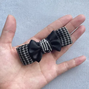 Macro detail of a handmade black and white tweed hair clip with a sleek satin bow accent