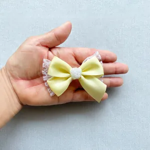 Macro shot of a yellow satin bow with white lace edges and a rose detail held by hand