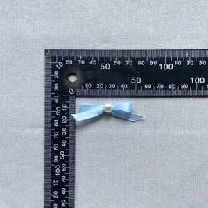 Detail of light blue ribbon bow with white pearl centerpiece measured on a ruler