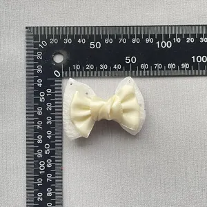 Detailed top view of a 6cm beige satin bow with lace and rhinestones next to a ruler