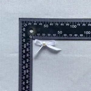Detailed view of handmade white ribbon bow with pearl center on metric measuring tool