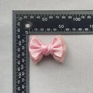 Close-up of pink satin bow with lace backing and rhinestones showing 6cm scale detail