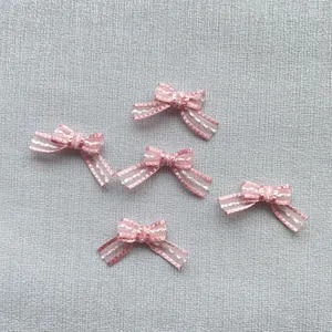Macro shot of 1.5cm pink satin bows with white stitched edges for DIY crafts