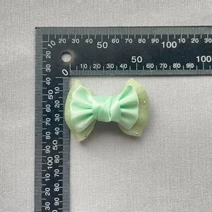 Light green double-layered bow accessory with rhinestones shown against a measuring scale