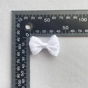 Detalle de un pequeño lazo de malla blanca con pedrería plateada sobre una regla de medida