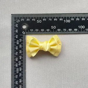 Close-up of yellow satin bow accessory with mesh edges showing size dimensions on a scale