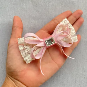 Dettaglio di un fiocco in pizzo rosa e bianco con gemma di cristallo in mano