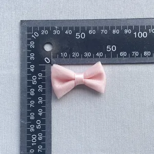 Close-up of pink satin bow hair accessory showing dimensions on a ruler