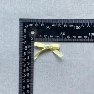 Detailed view of small light yellow ribbon bow with pearl core and size measurement