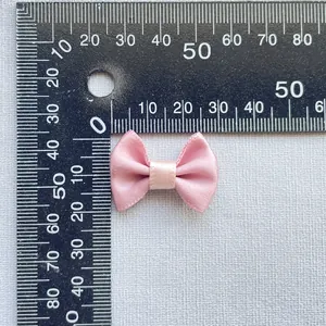 Macro view of a 3cm pink satin ribbon bow accessory displayed on a white textured cloth