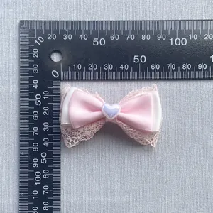 Handmade pink lace ribbon bow accessory with heart bead shown with ruler for size