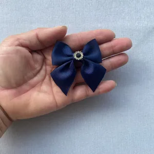Macro shot of mini navy grosgrain bow with rhinestone center held in hand for scale
