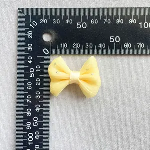 Vista detallada del pequeño lazo de organza amarilla con medida de 45 mm en regla
