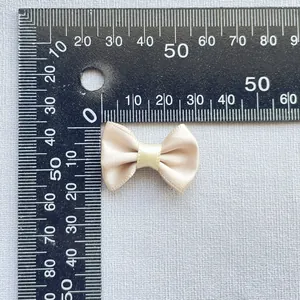 Detail view of 30mm champagne satin bow accessory measured with a ruler for scale