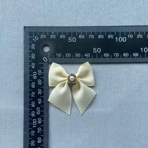 Cream grosgrain ribbon bow with pearl and rhinestone center on a gray background