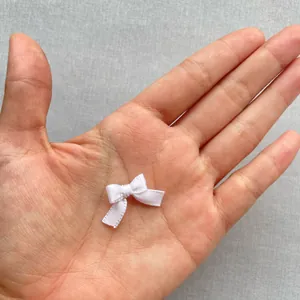 Mini lazo de satén blanco en la punta del dedo mostrando el tamaño de 1,5 cm para manualidades