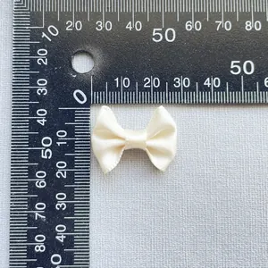 Close-up of 3cm ivory satin ribbon bow accessory measured with a ruler for DIY crafts