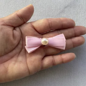 Detail of pink silk ribbon bow with faux pearl center held in hand for size scaling