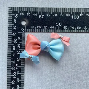 Detail einer rosa und blauen Satinschleife mit Mini-Strassknoten auf grauem Hintergrund