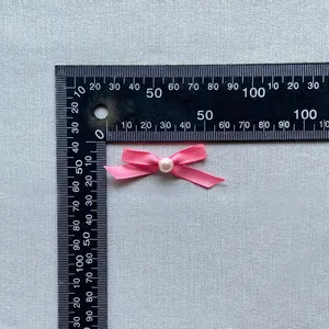 Detailed close-up of a pink satin bow with a white pearl bead decoration and size scale