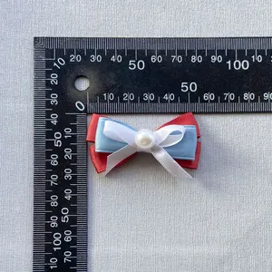 Detalle de lazo de cinta de tres capas de 5 cm con perla junto a una regla graduada